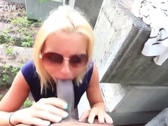 Petite blonde cock teaser is wearing sunglasses while sucking a black dick outdoor, during the day